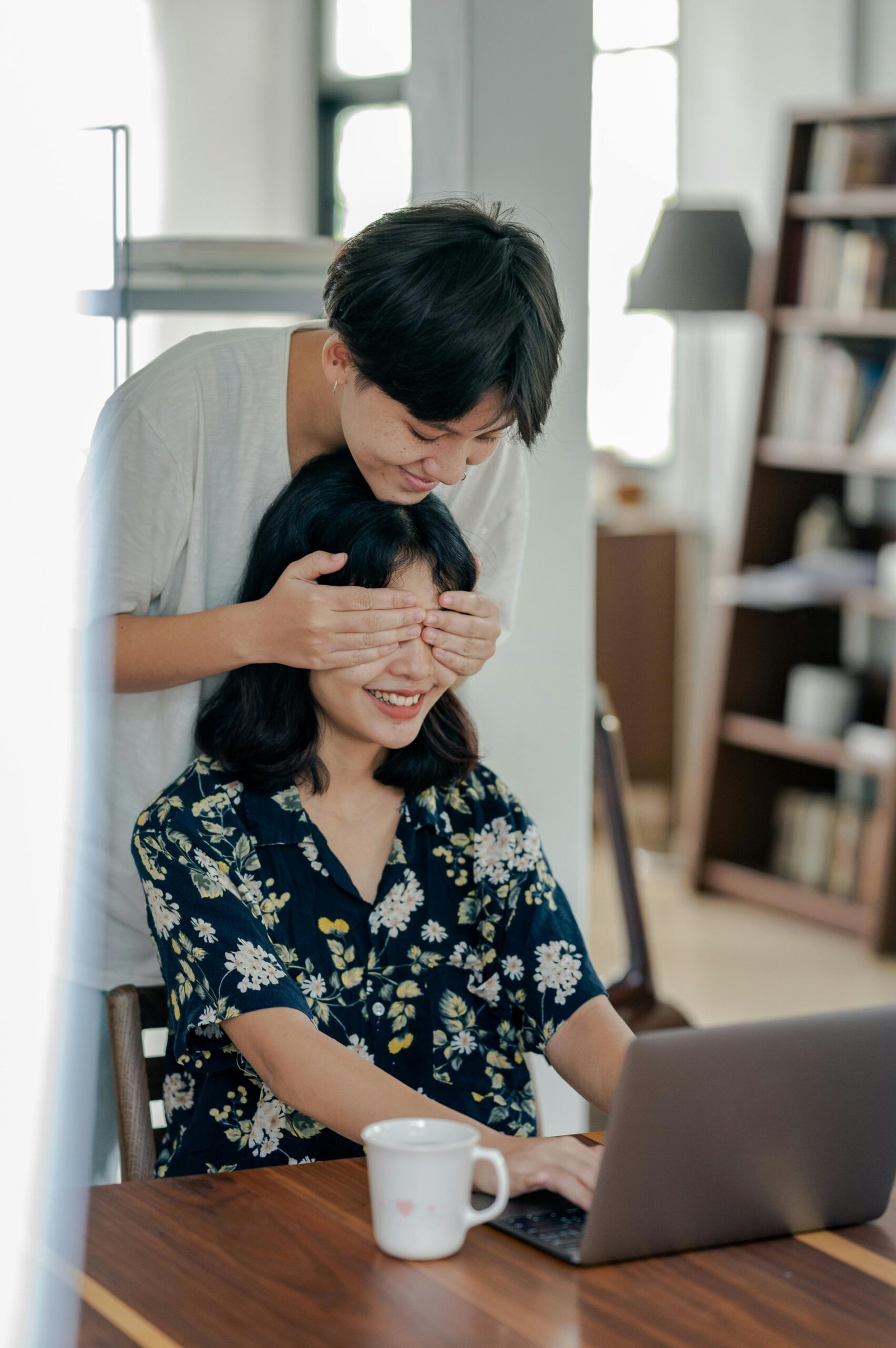 Two women enjoying a playful moment by covering eyes with joy in a cozy home office.